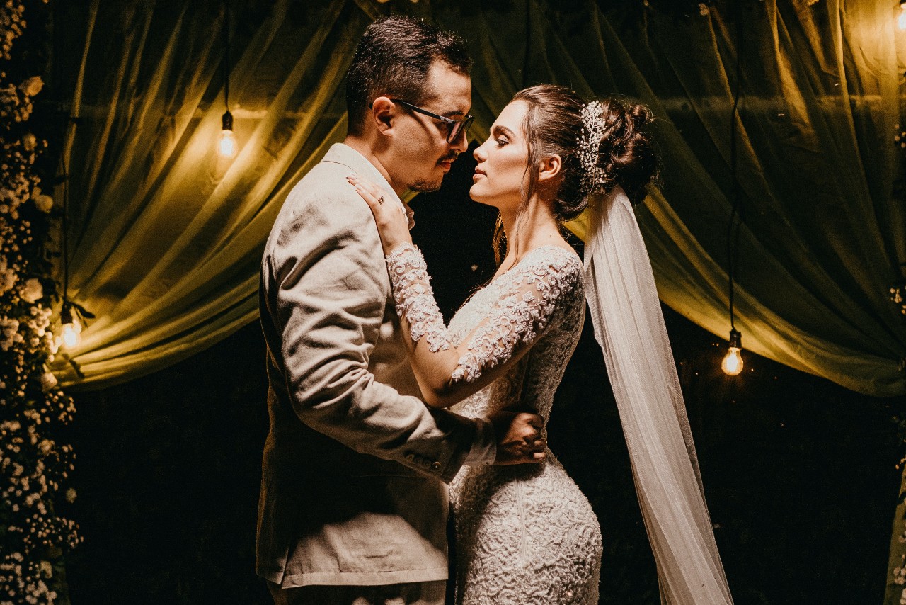 a bride and groom embracing in front of curtains in a dimly lit room