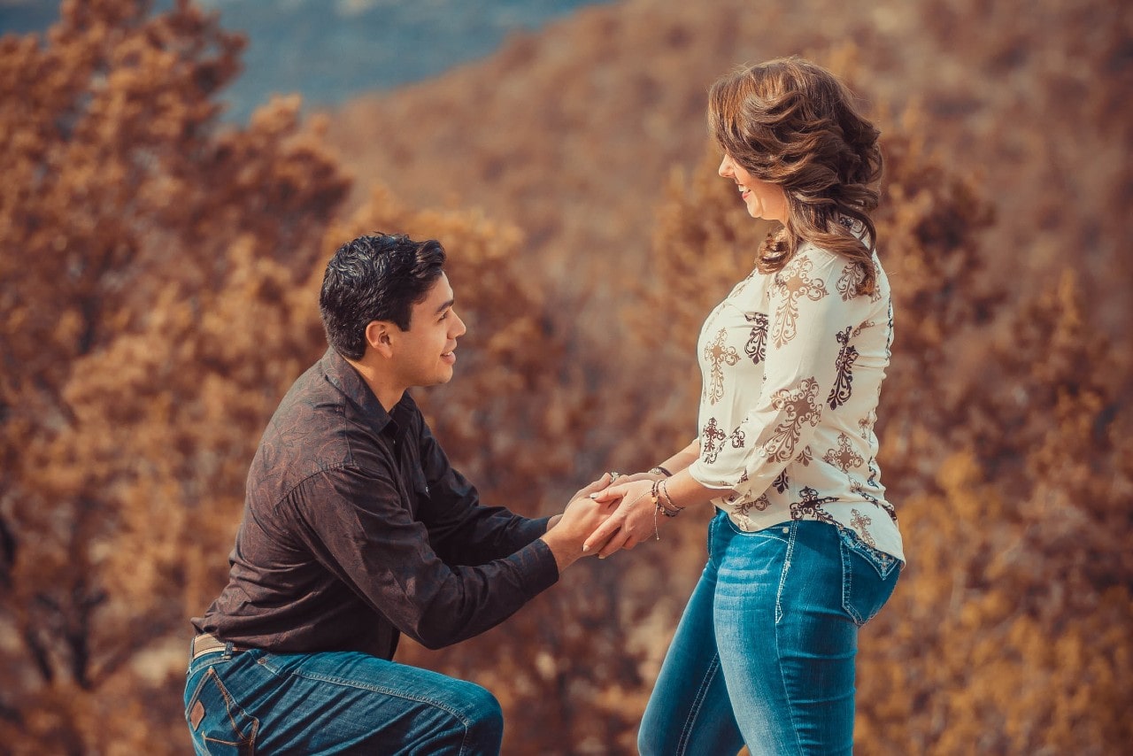 a man standing on one knee proposing to a lady with a nature background