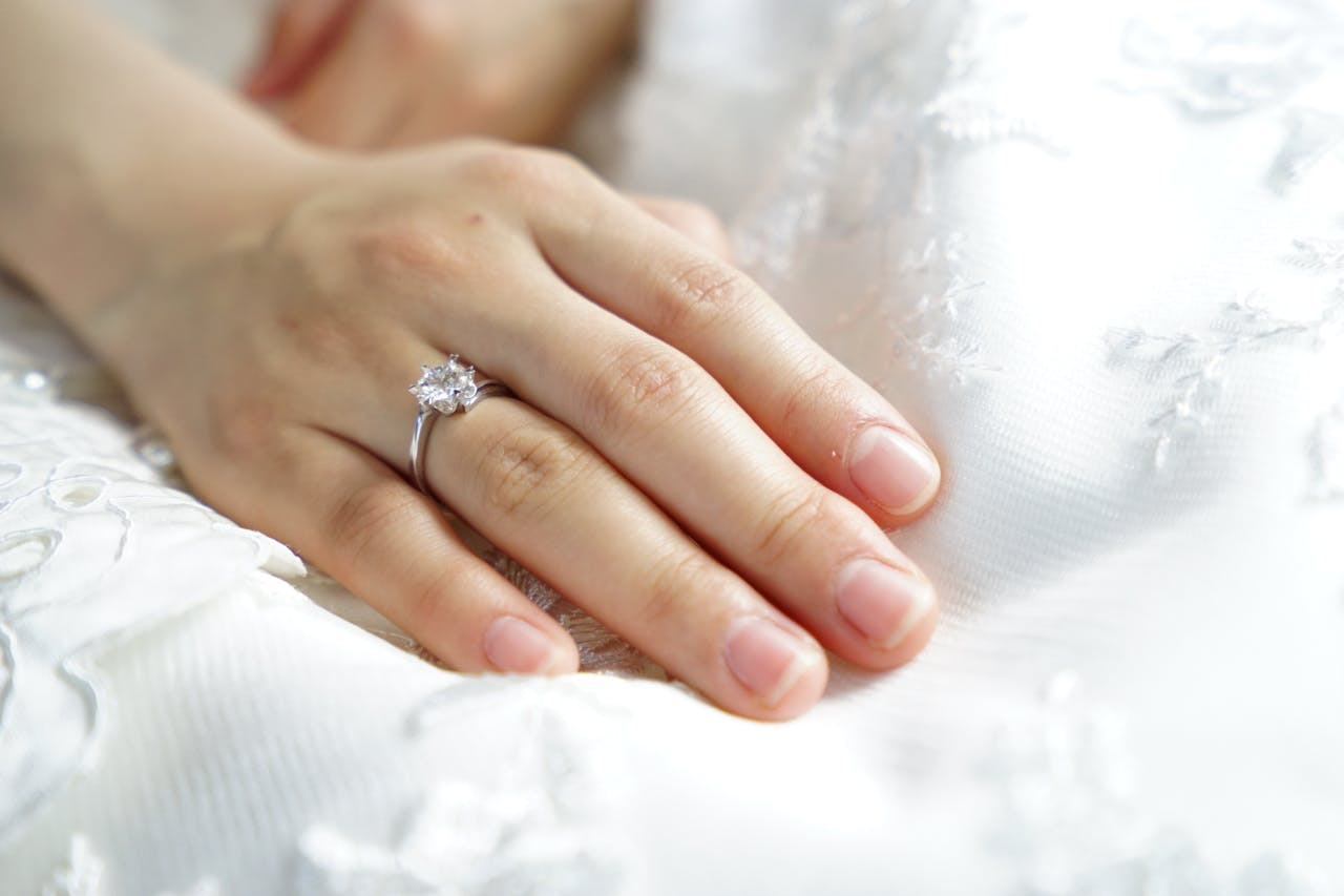 A close up of bride&rsquo;s hand in a white gold diamond engagement ring on top of the white fabric