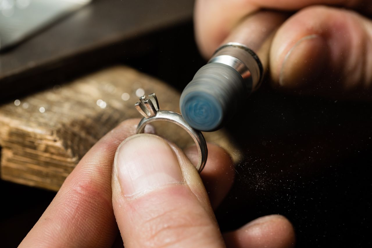 A close up of a jeweler sanding a silver engagement ring with a drill.