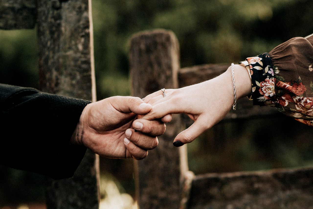 A close up of a couple holding hands with a woodsy background.