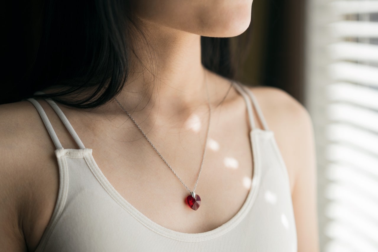 close up image of a woman looking out a window and wearing a red heart pendant necklace