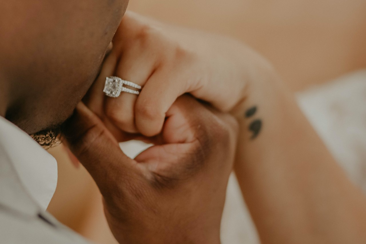 A man kisses his fiancee’s hand, showing off her halo engagement ring.