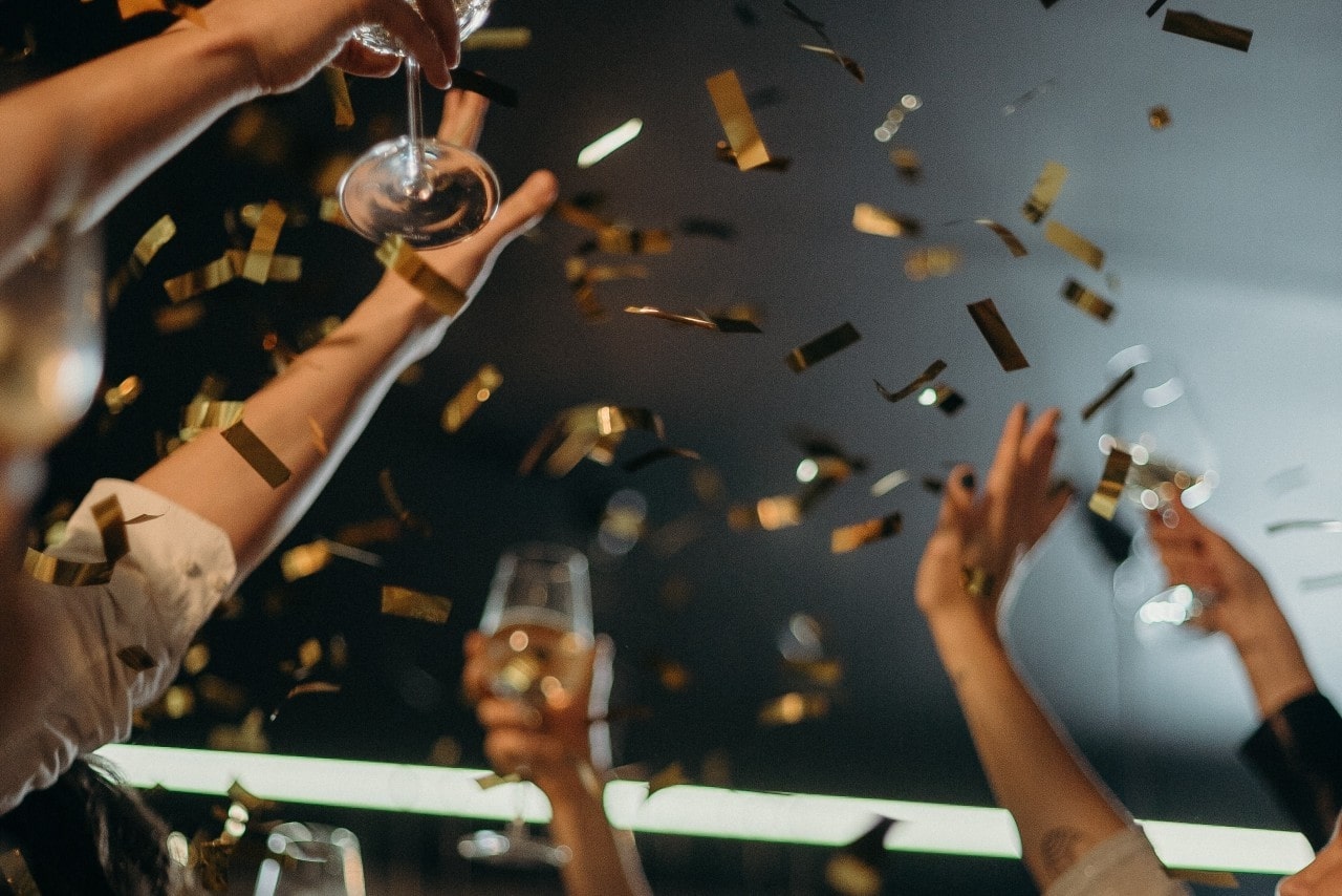 a group of arms holding up glasses with confetti in the air