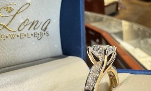 A close-up of an elegant side stone engagement ring displayed in an open box with Long Jewelers embossed on the underside of the top.