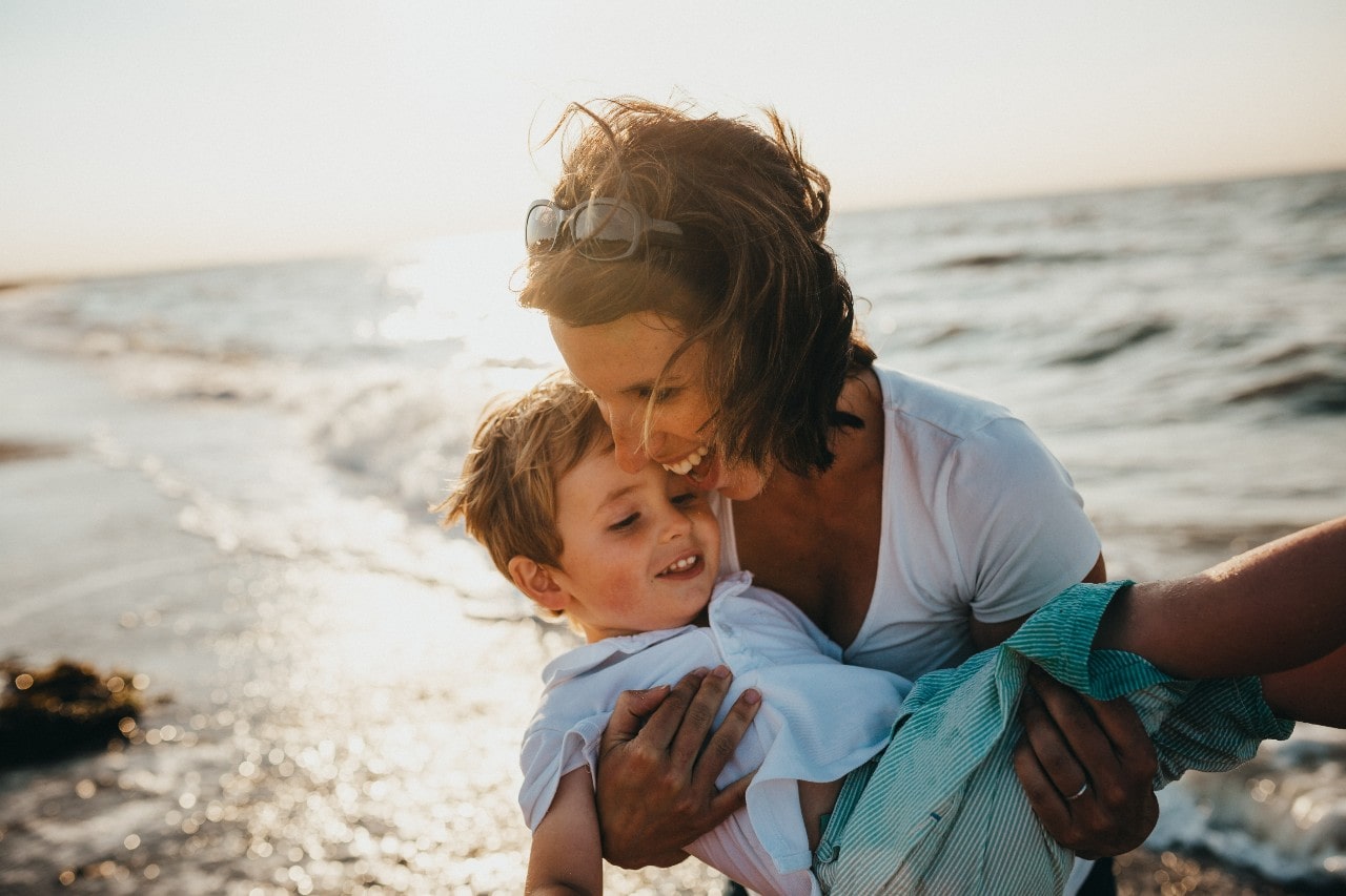 A mother holding her son in her arms on a sunny day at the beach.
