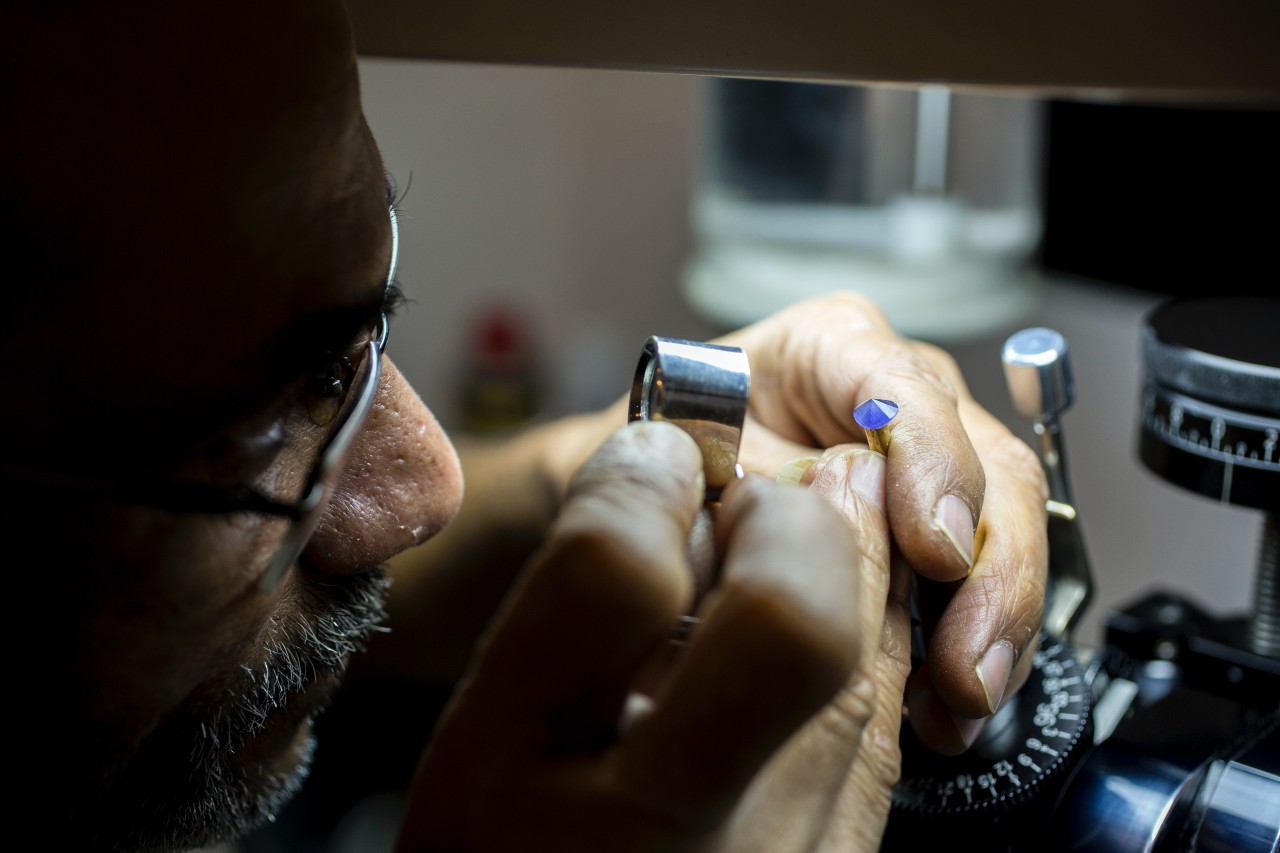 A jeweler examines a gemstone under a magnifying glass, focusing intently.