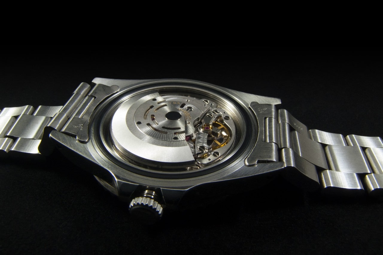 A close up of a metallic wristwatch placed upside down, showcasing its gears.