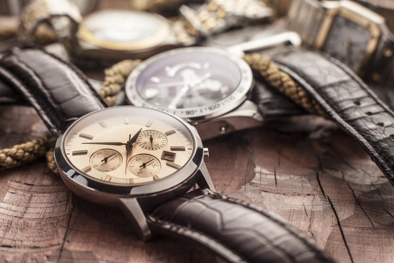 A macro shot of luxury wristwatches with leather straps laid out on a rustic wooden surface, highlighting detailed dials and textures.
