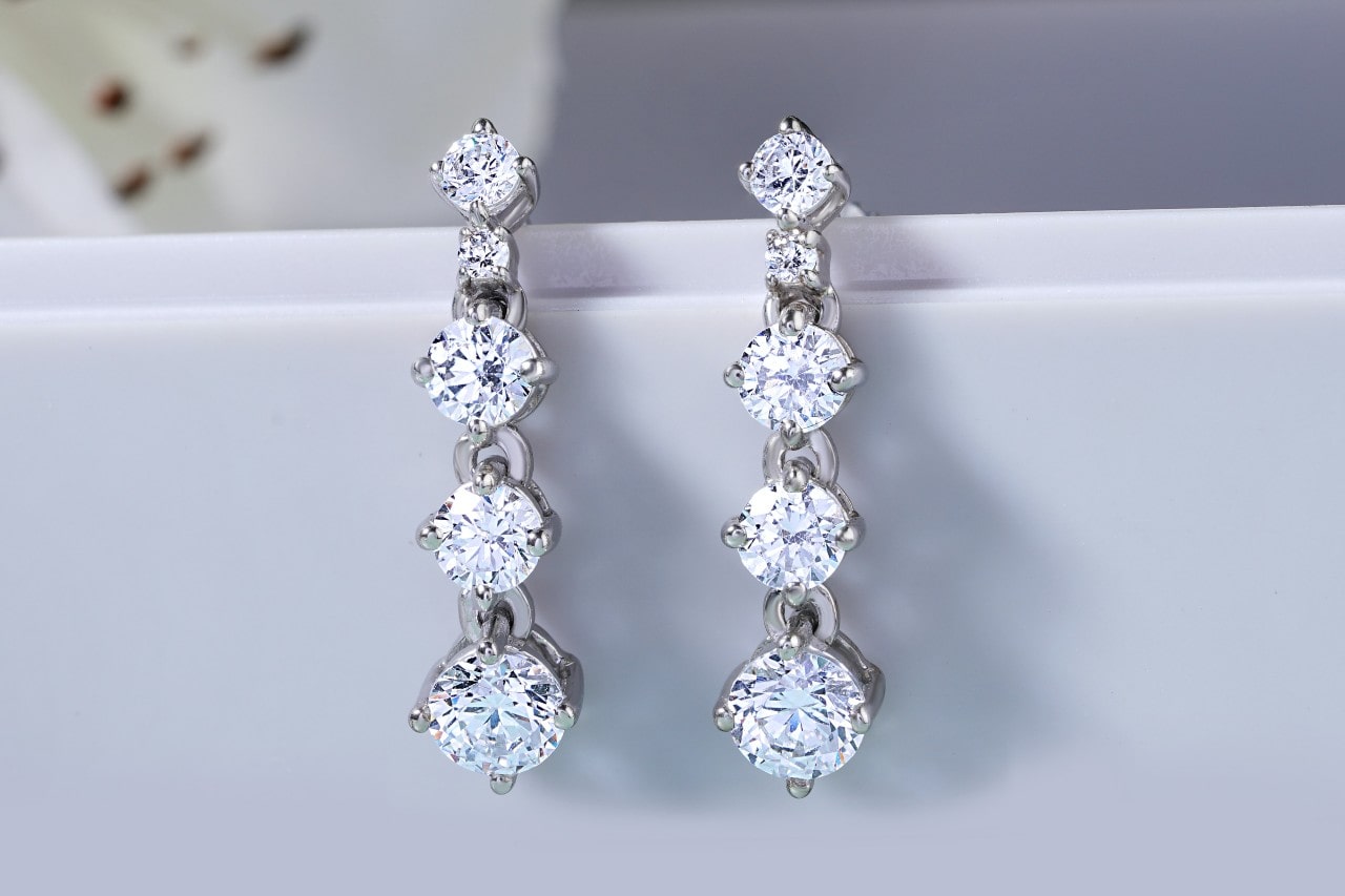 a pair of tiered diamond drop earrings hanging off of a white surface