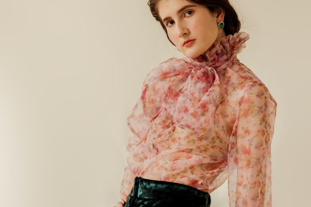 a woman in a floral blouse posing wearing green gemstone stud earrings