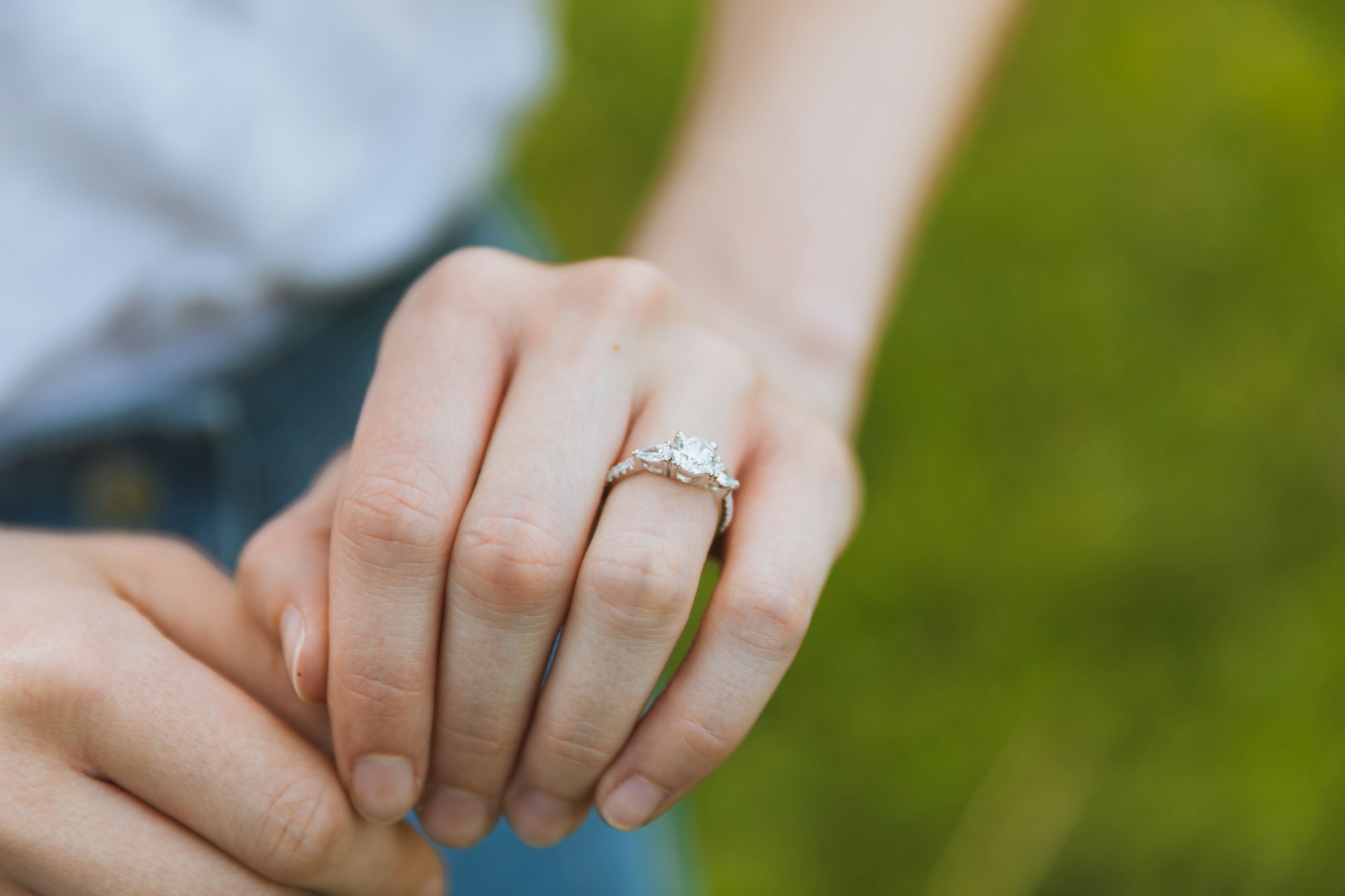 A close up of side stone ring on a woman’s hand against a blurry grass background