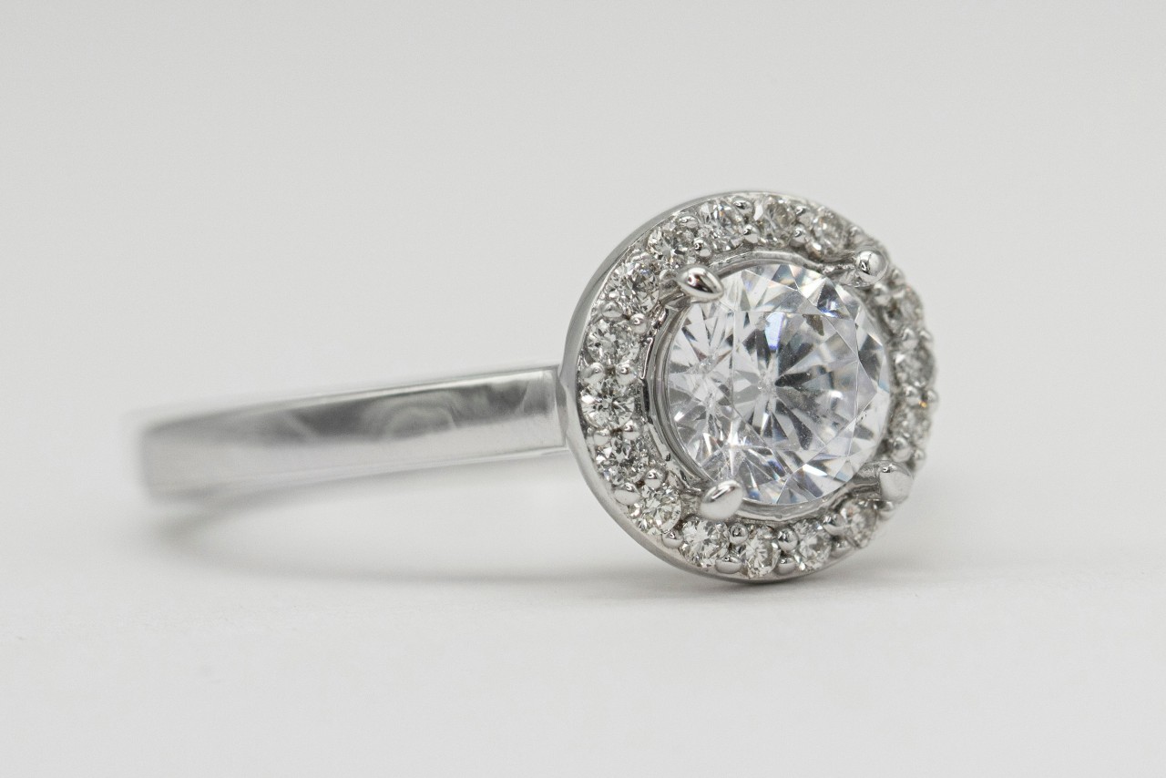 A white gold halo engagement ring with a large round brilliant-cut centre diamond surrounded by a circle of smaller diamonds.