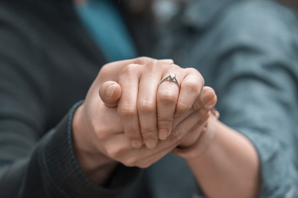 Close-up of a couple holding hands, with an emphasis on the woman's glistening solitaire engagement ring.