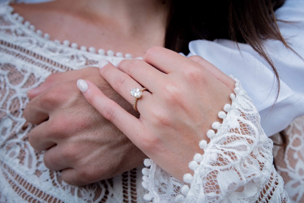 a lady’s hand wearing an engagement ring resting over a man’s