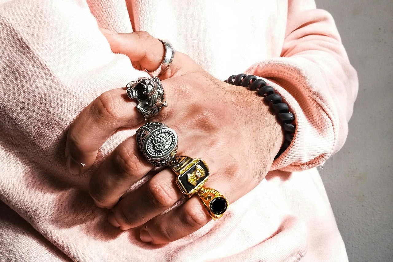 A close-up of a man’s hand wearing multiple ornate rings, including silver and gold designs.