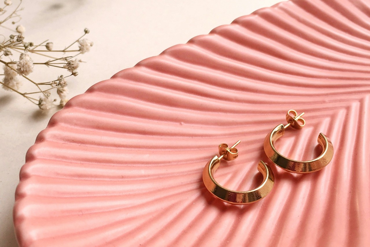 a pair of yellow gold huggie earrings sitting on a pink dish a pair of yellow gold huggie earrings sitting on a pink dish