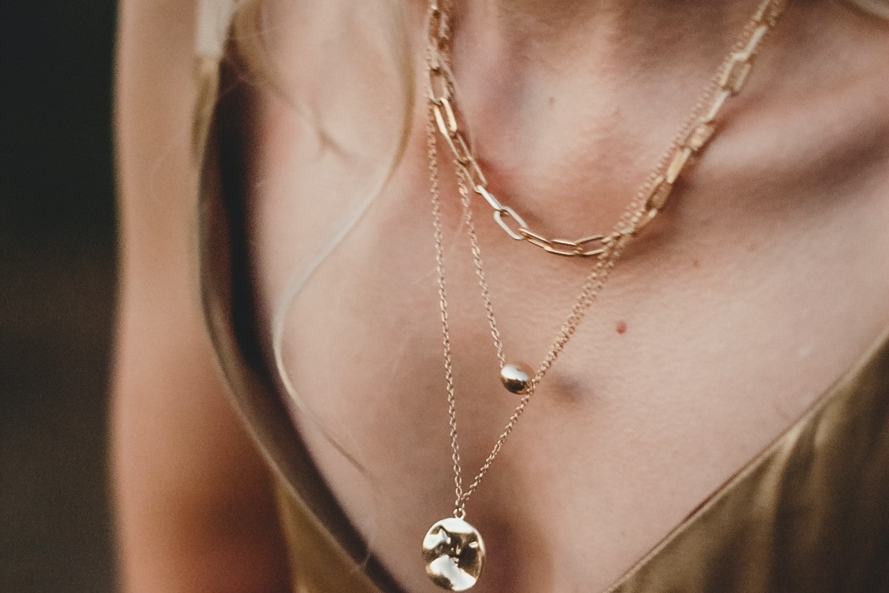 a close up image of a woman’s neckline, adorned with three gold necklaces