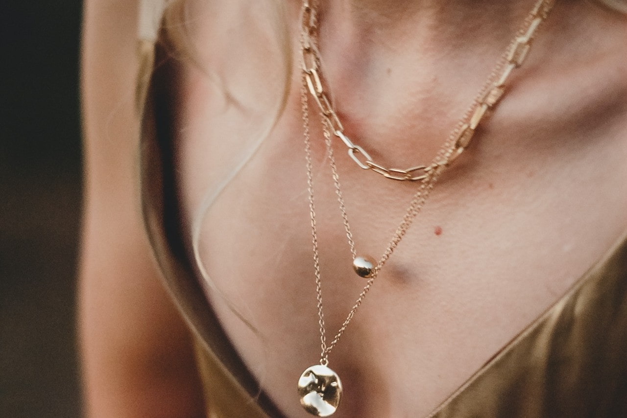 a close up image of a woman’s neckline, adorned with three gold necklaces a close up image of a woman’s neckline, adorned with three gold necklaces