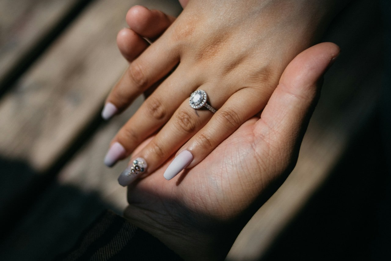 Close up of a couple’s hands adorned with a sparkling halo engagement ring.