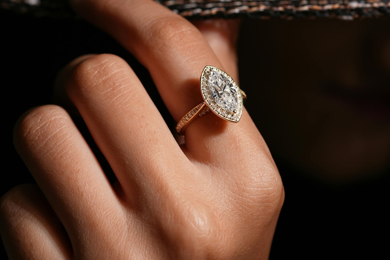 Close-up of a hand wearing a beautiful marquise halo ring with a pavé diamond band.