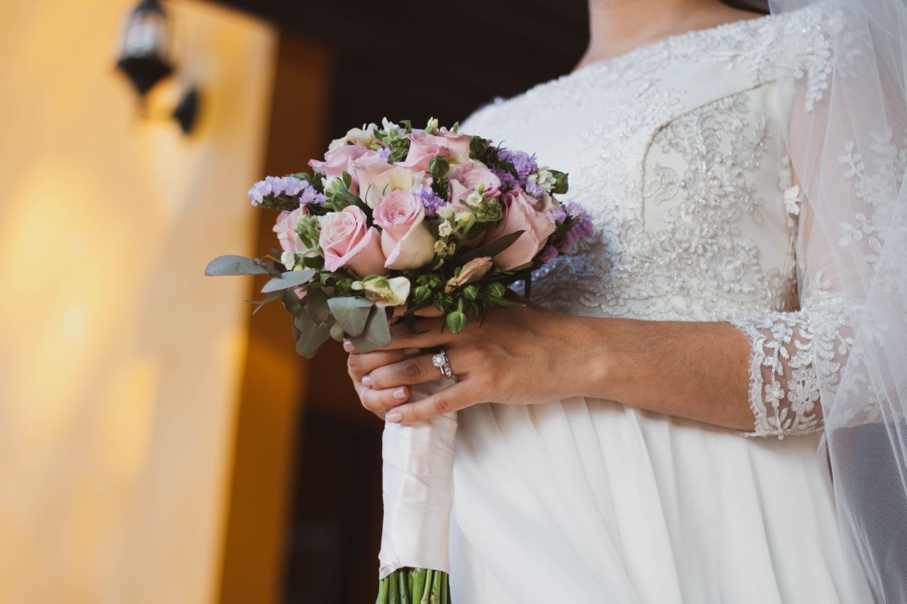 wedding ring and engagement ring on woman’s hand holding flowers wedding ring and engagement ring on woman’s hand holding flowers