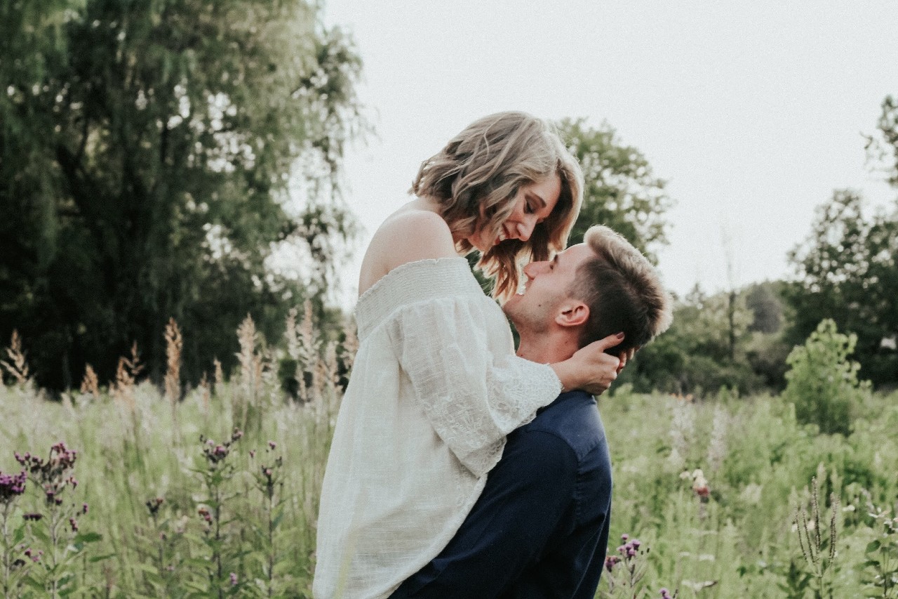 A couple embraces intimately in an overgrown field.
