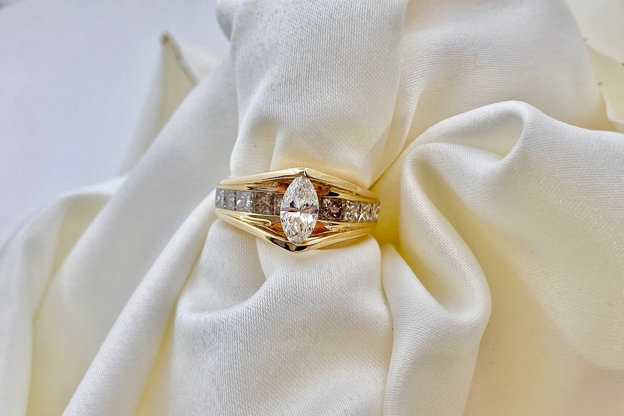 a large marquise-cut diamond ring sits among cream-colored fabric.
