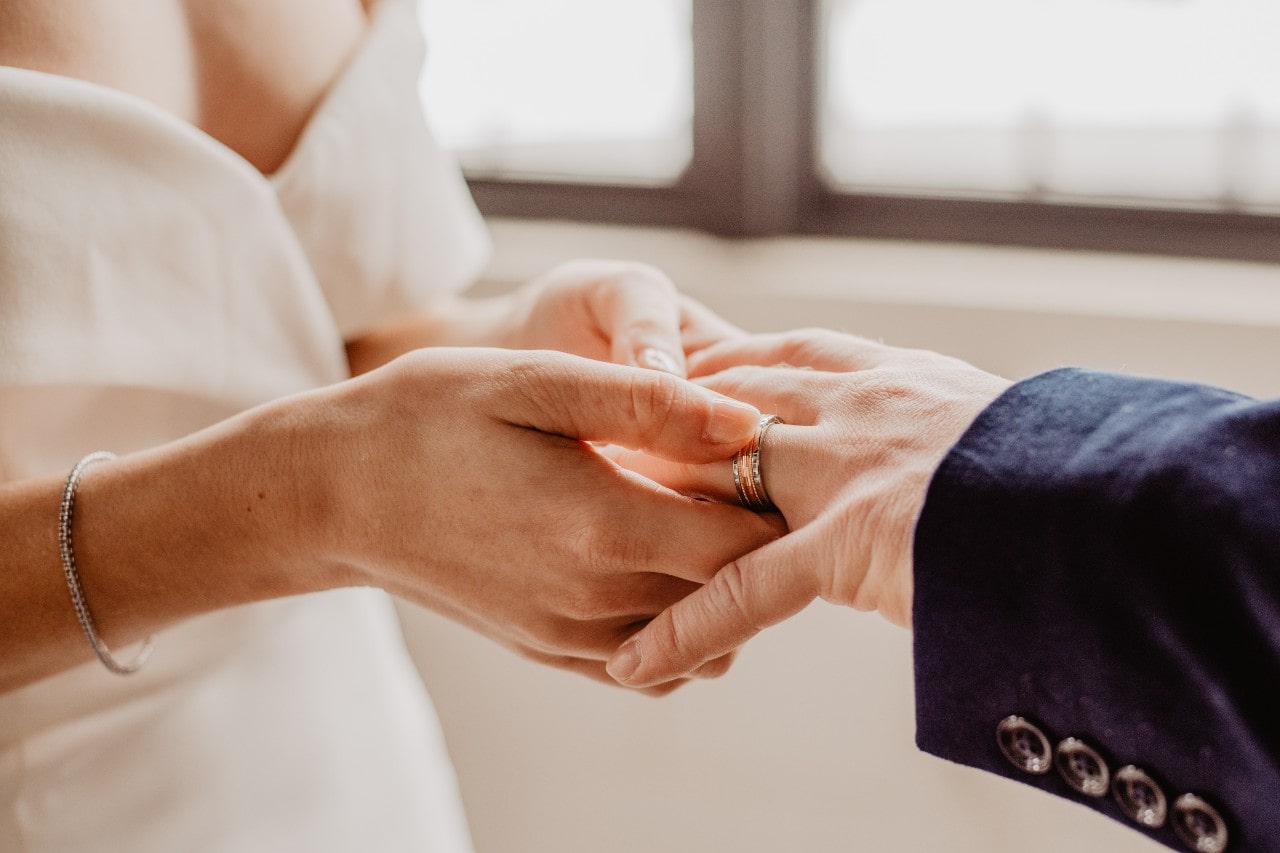 a bride sliding a mixed metal wedding band onto her groom’s hand a bride sliding a mixed metal wedding band onto her groom’s hand