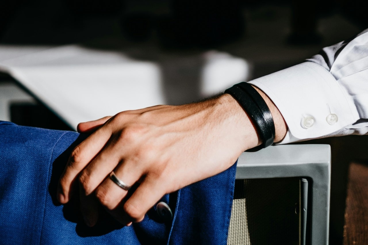 a man’s hand resting on the back of a chair, adorned with a silver wedding band a man’s hand resting on the back of a chair, adorned with a silver wedding band