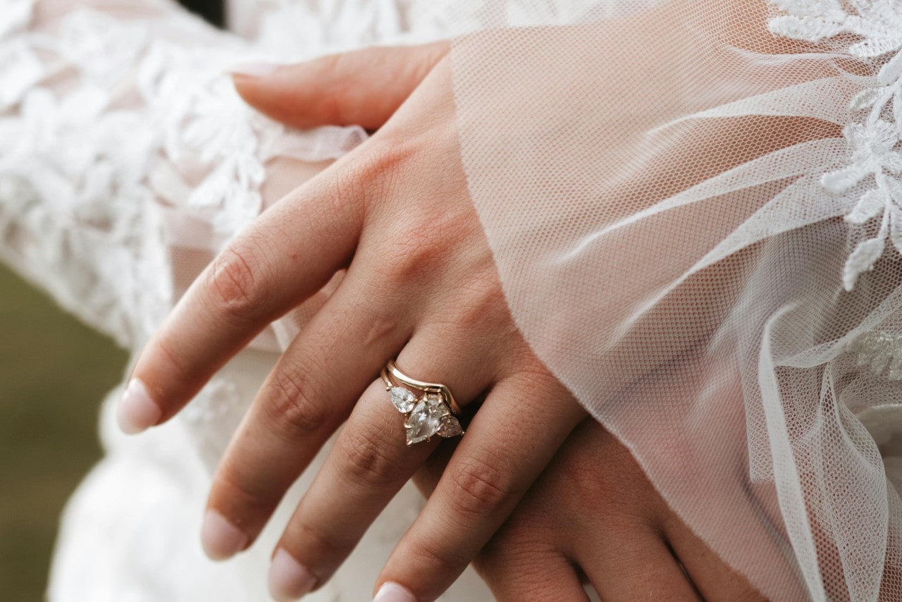 A close-up of a yellow gold three-stone pear shape engagement ring and a complimentary yellow gold band on a woman’s hand.
