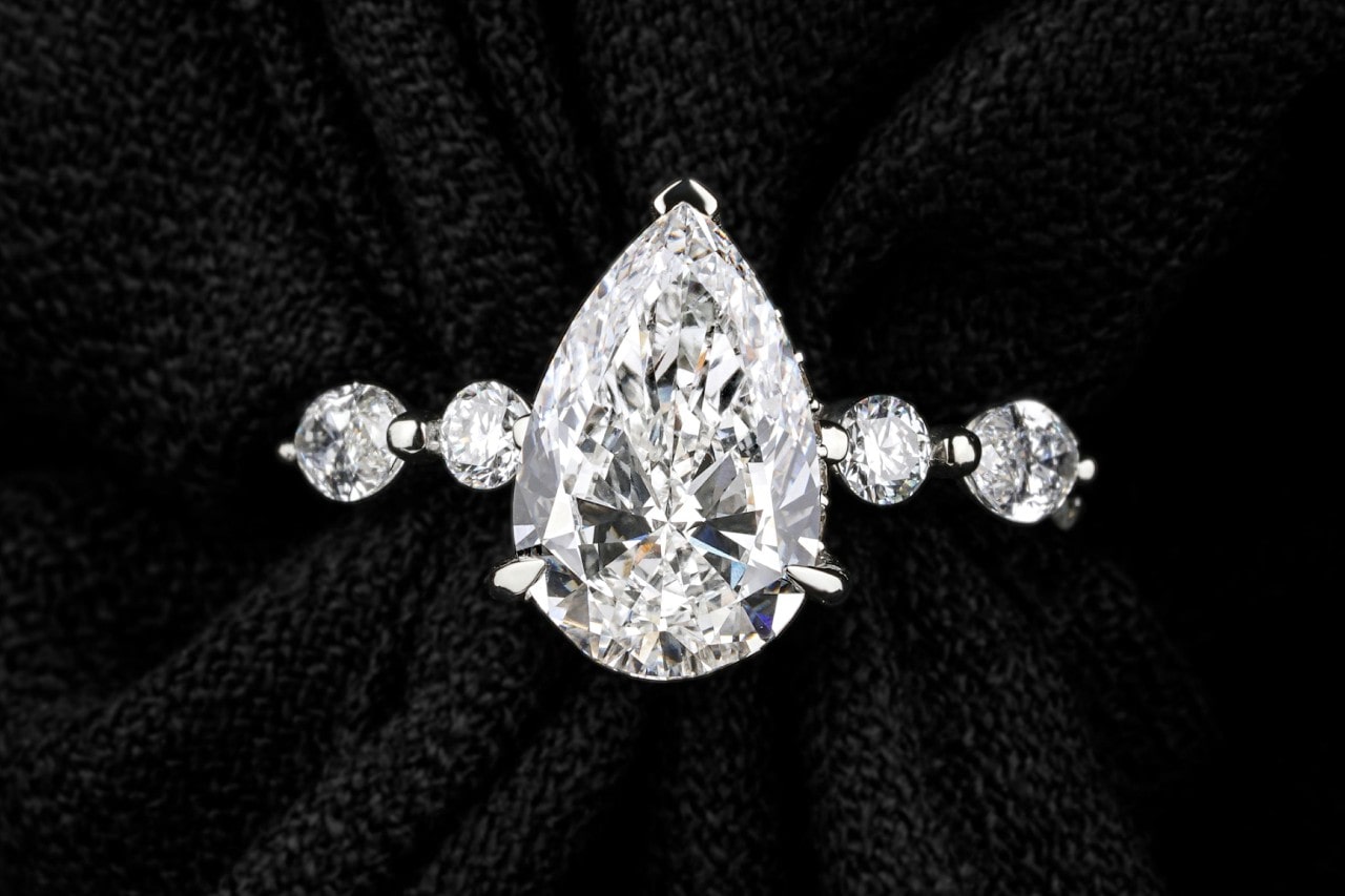 A pear shape engagement ring with diamonds along the band tucked into a black fabric.