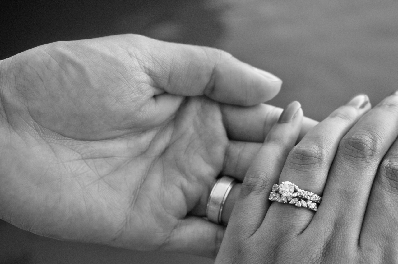 a black and white photo of two hands wearing bridal rings a black and white photo of two hands wearing bridal rings