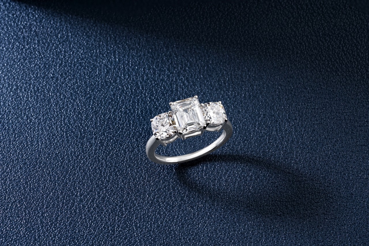 A white gold three stone diamond engagement ring on a deep blue textured surface.