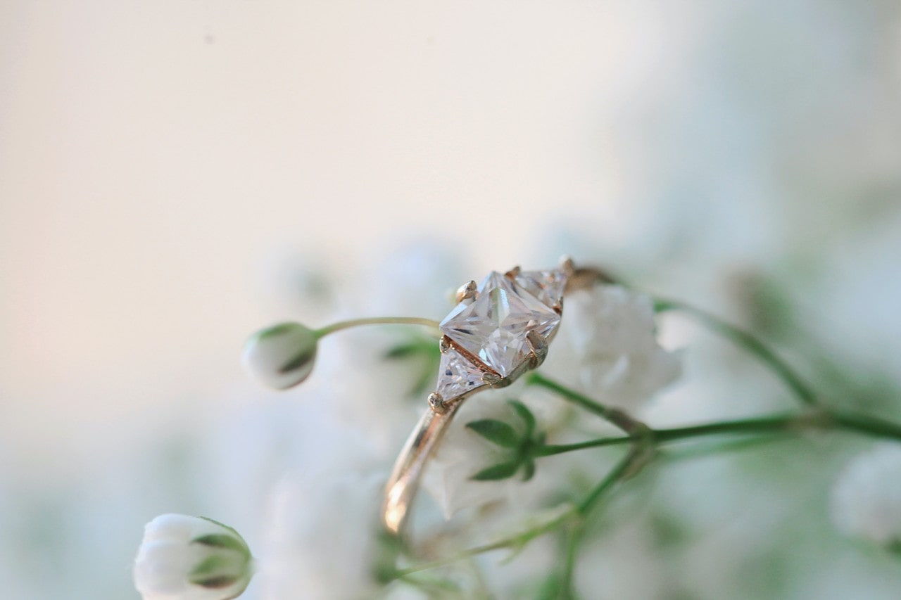 A close up of a yellow gold three stone engagement ring on small white flowers.