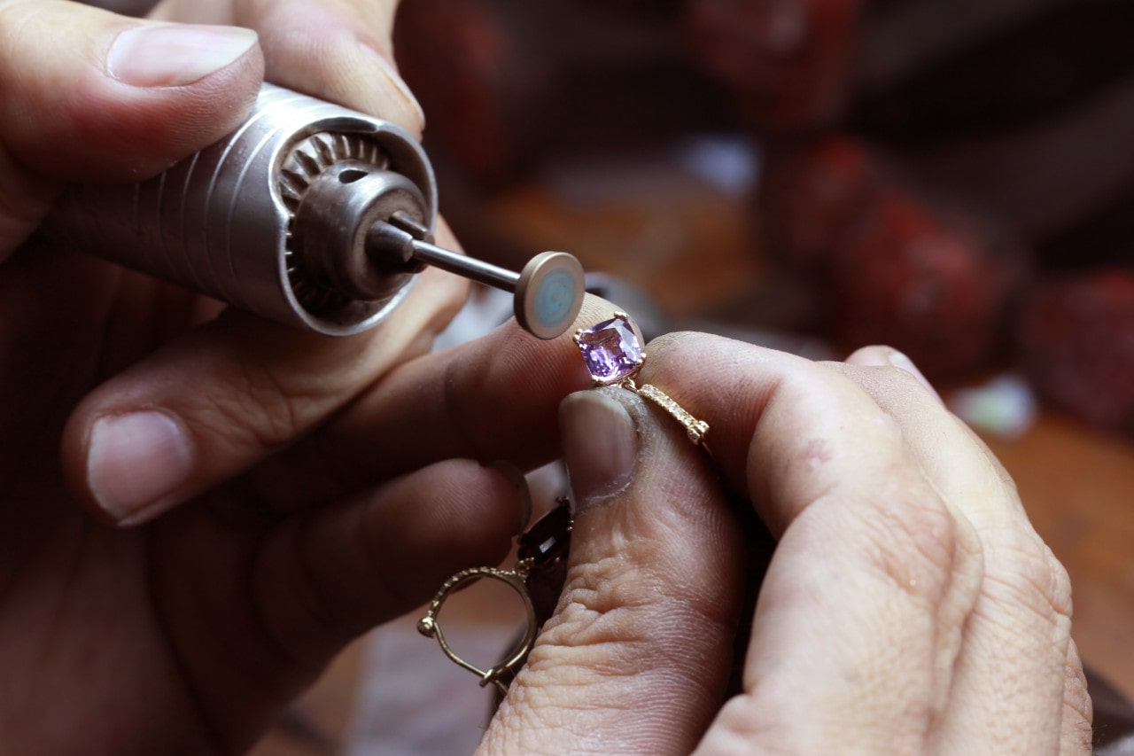 A gemologist inspects a pink gemstone on a pair of yellow gold earrings.