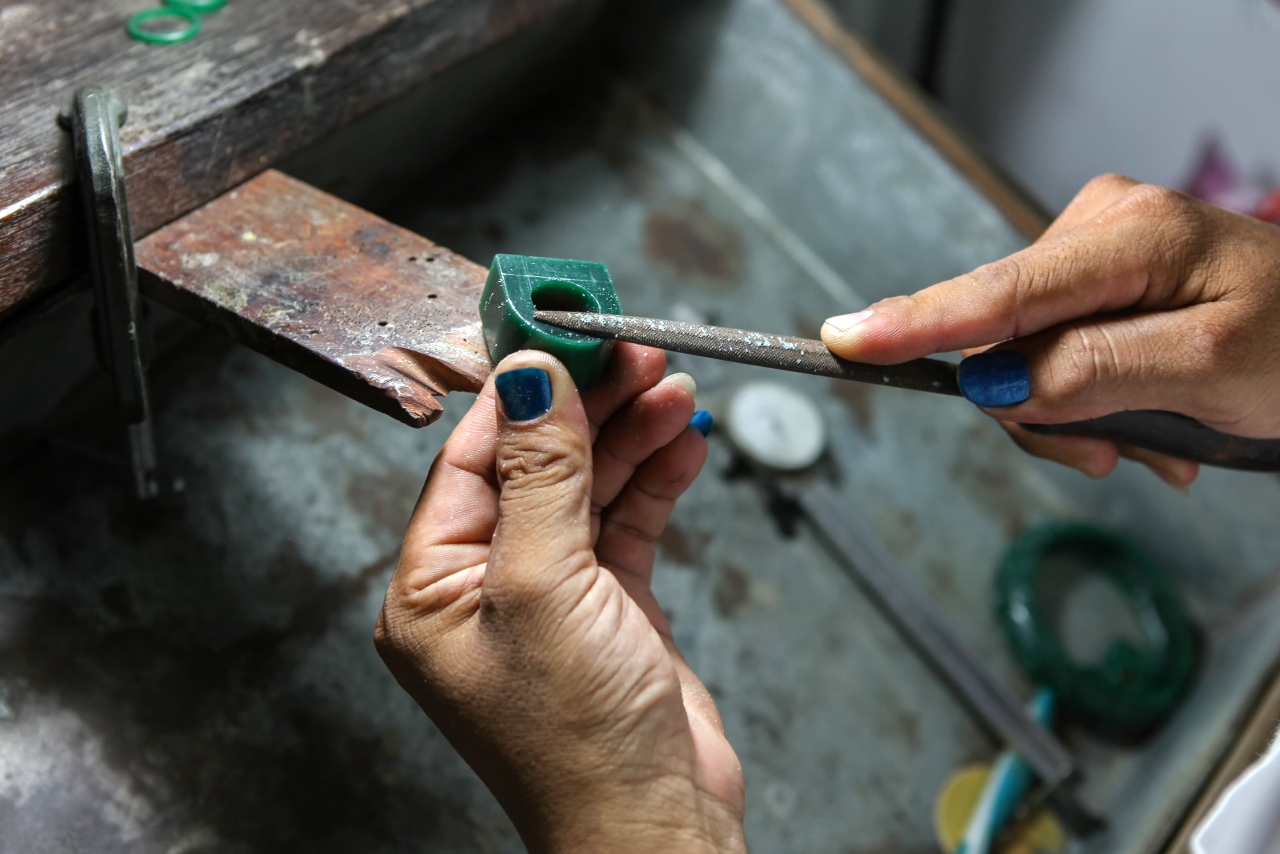 Hands carefully file a green wax ring model at a jeweler’s bench, shaping the design before it is cast into metal.