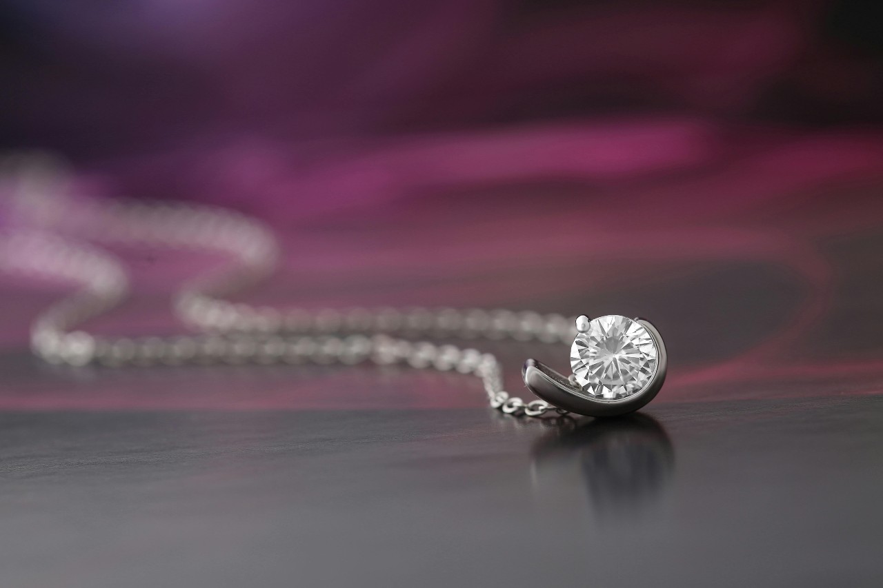 A close-up of a simple yet elegant diamond pendant necklace on a dark background. A close-up of a simple yet elegant diamond pendant necklace on a dark background.