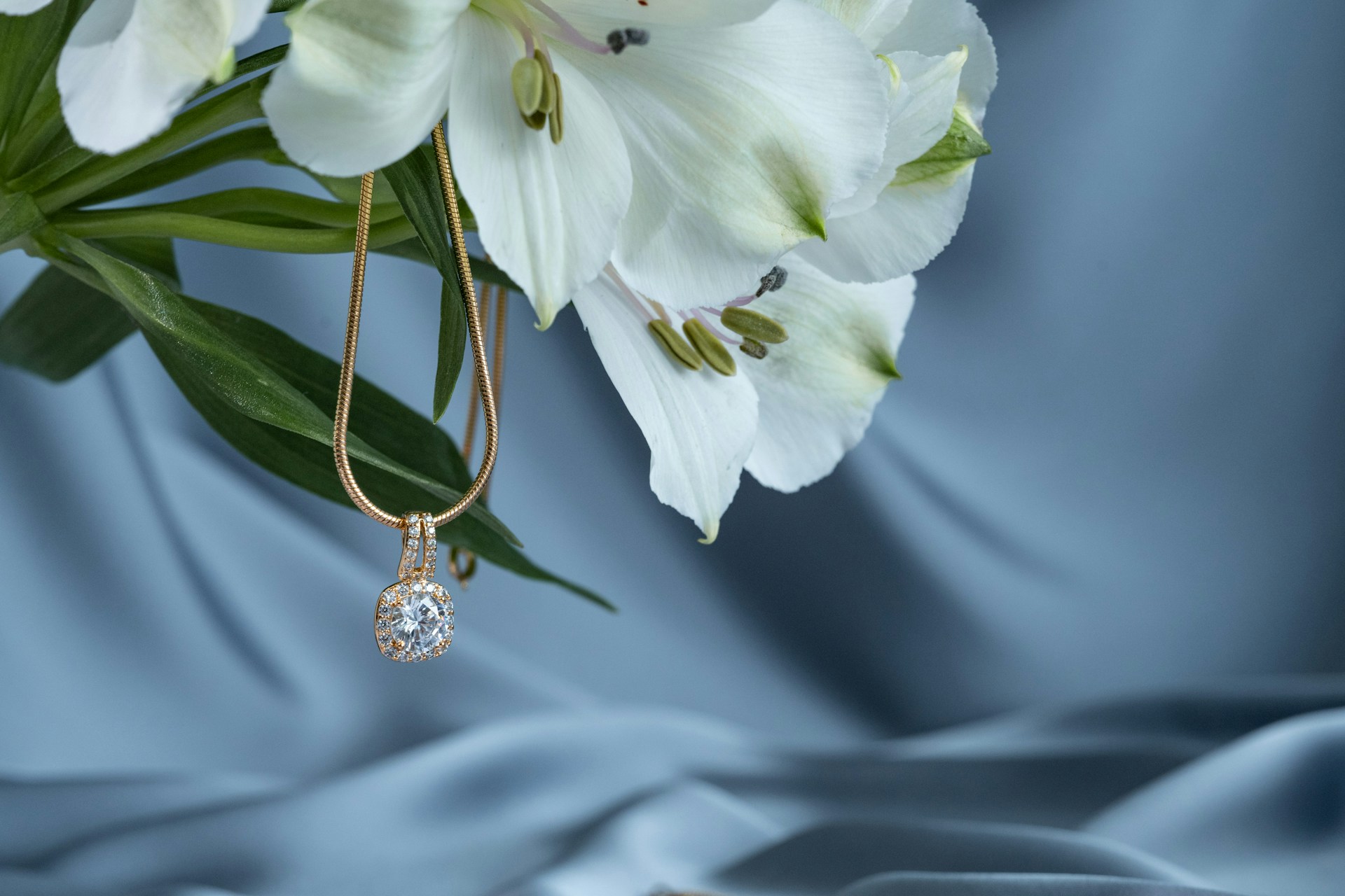 A close-up of a diamond pendant necklace draped from elegant lilies. A close-up of a diamond pendant necklace draped from elegant lilies.