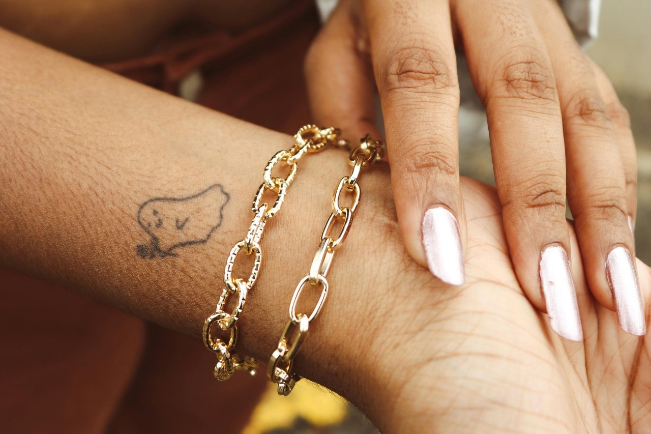 A close-up of a woman’s wrist, adorned in two gold chain bracelets. A close-up of a woman’s wrist, adorned in two gold chain bracelets.