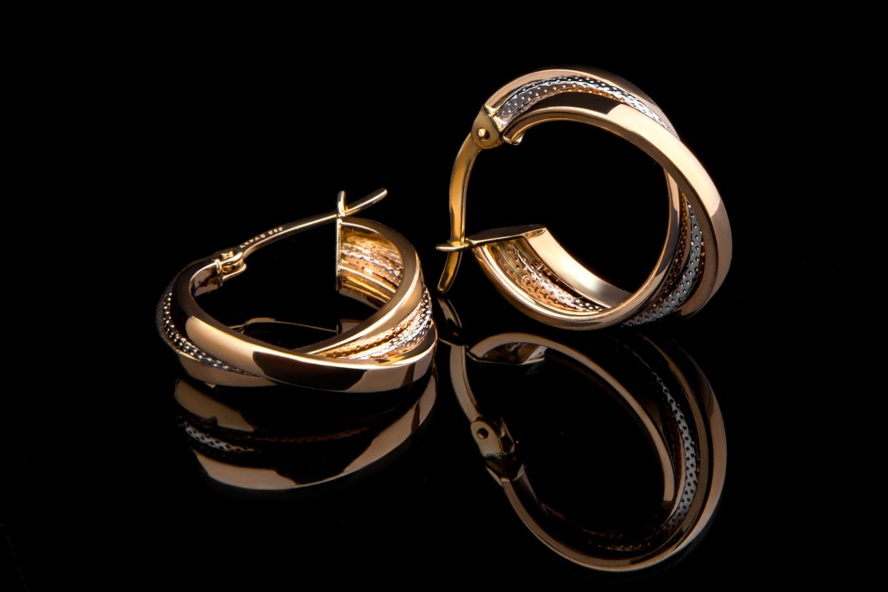 A pair of gold hoop earrings on a black surface. A pair of gold hoop earrings on a black surface.