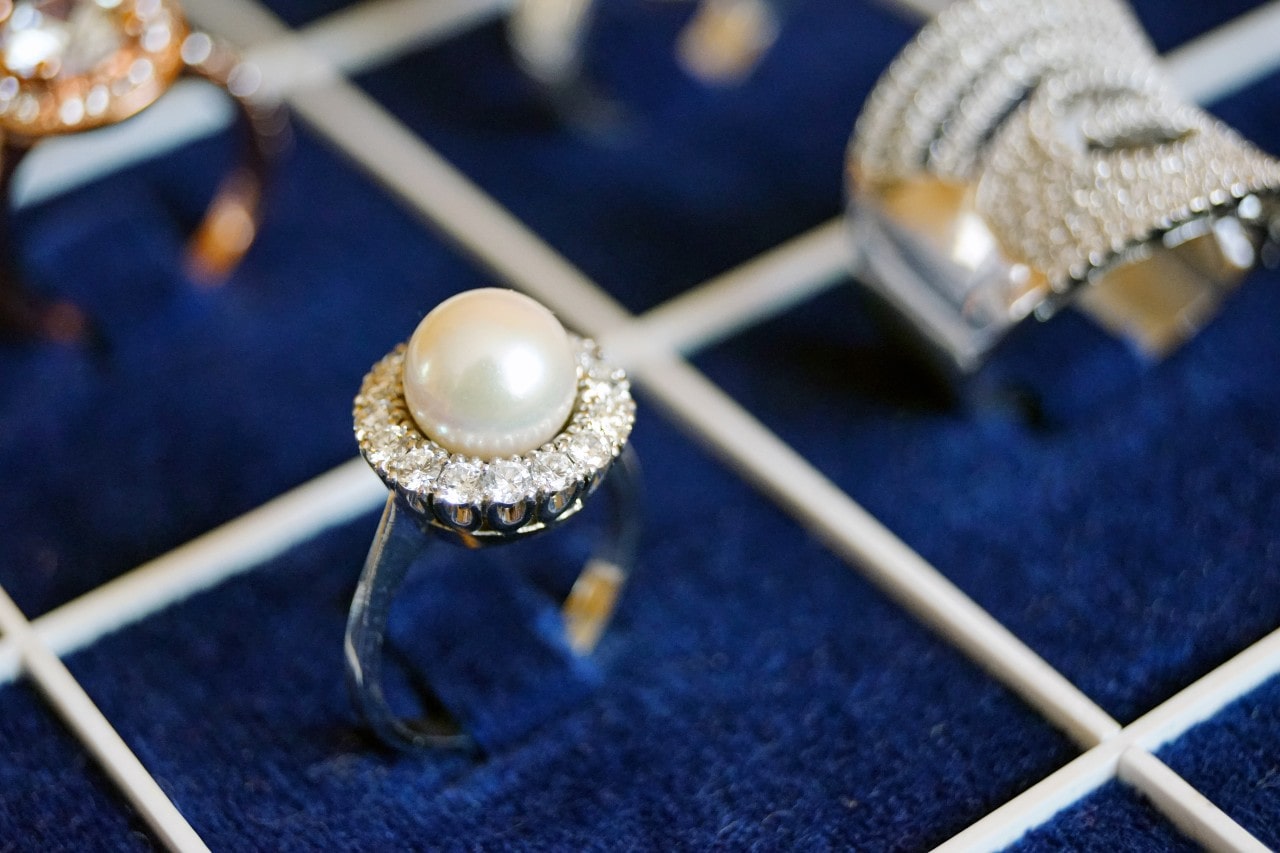 A close-up of dazzling fashion rings, with emphasis on a halo ring with a pearl center stone. A close-up of dazzling fashion rings, with emphasis on a halo ring with a pearl center stone.