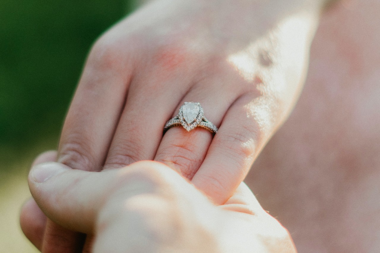 Close-up of a hand with an split band elegant pear-shaped diamond ring, held gently by another hand. Close-up of a hand with an split band elegant pear-shaped diamond ring, held gently by another hand.