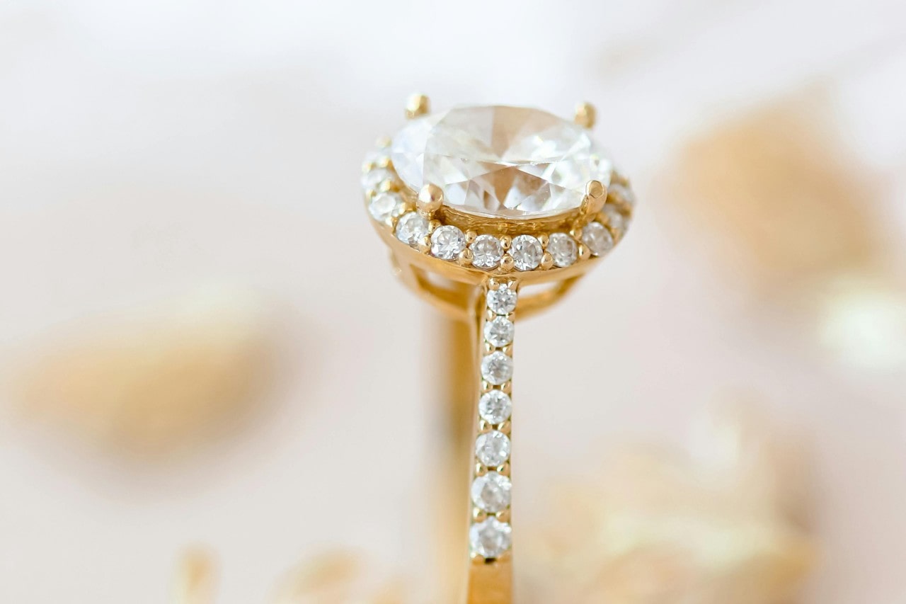 A close-up of a stunning gold engagement ring, with side stones and a halo setting. A close-up of a stunning gold engagement ring, with side stones and a halo setting.